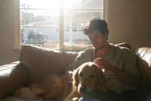 A man at a musical and arts themed sober living plays guitar with an older mentor on couch.